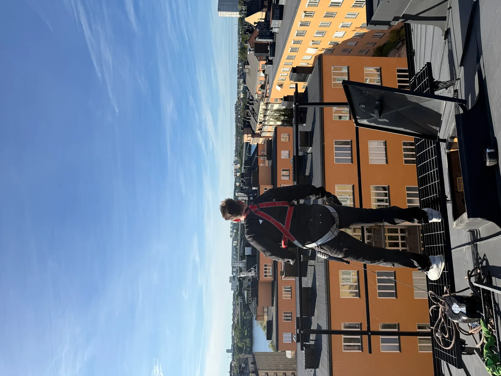En person med röd sele står på ett tak med stadsutsikt.