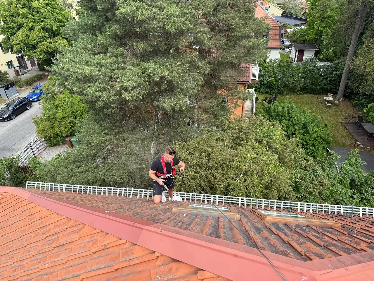 En takläggare med säkerhetssele arbetar på ett tegeltäckt tak.